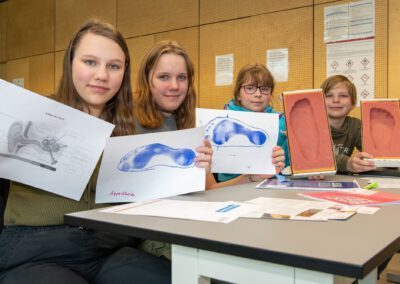 von links nach rechts: Anna-Marie Ott, Sophia Schilling, Isabel Möller, Maja Möller: stolze Teilnehmerinnen in einer der Werkstätten der Medizintechnik mit Fußabdruck und Zeichnung vom Aufbau eines Ohres